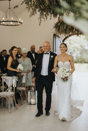 Wedding ceremony in a modern white venue with lanterns, chandelier, and floral decor hanging from the ceiling.
