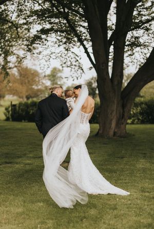 A romantic wedding photo of a couple dancing outdoors under a large tree with flowing white dress and veil.