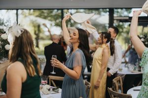 A group of wedding guests in formal attire dance and celebrate with raised arms at an outdoor reception.