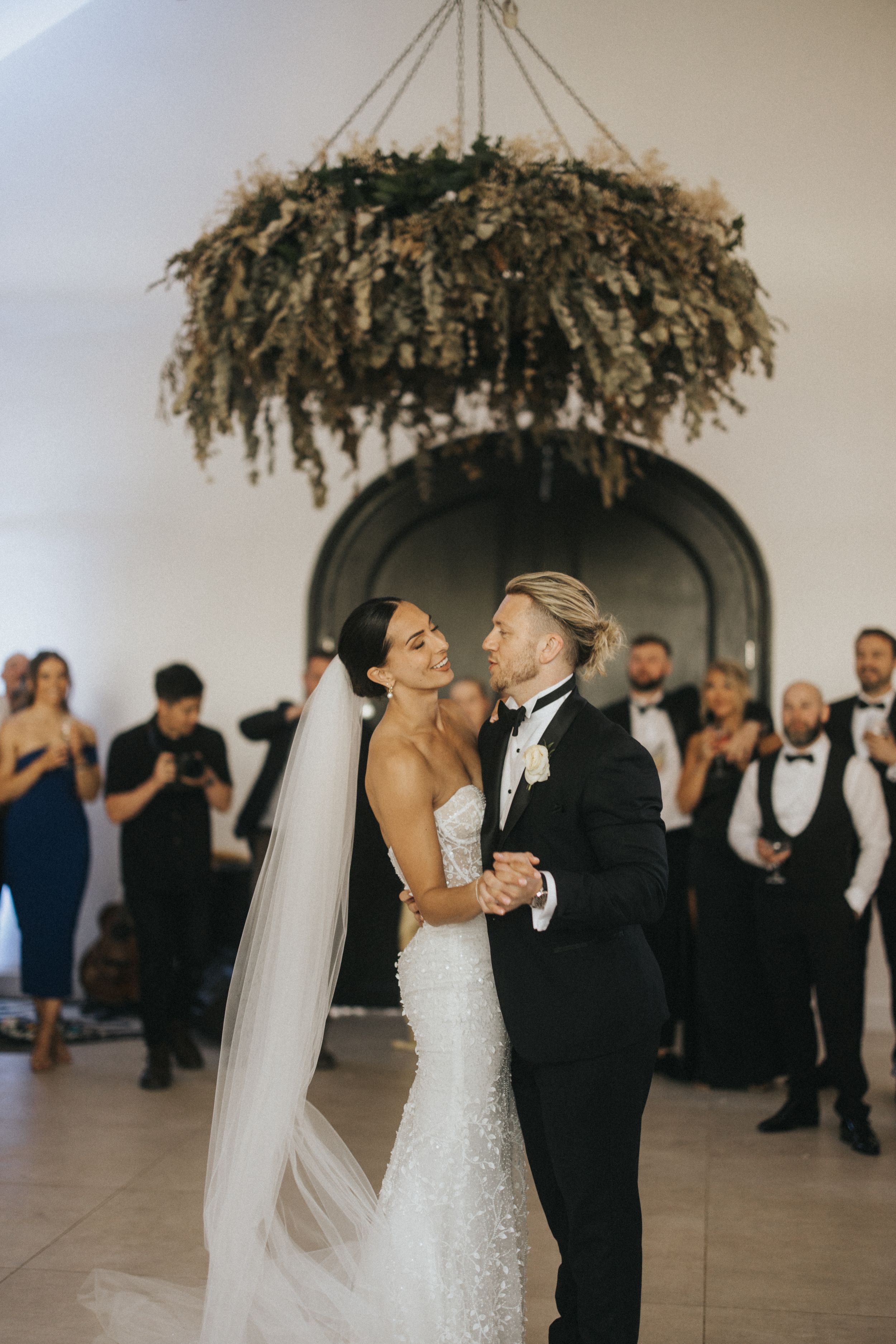 A couple shares their first dance under a dried flower chandelier at an elegant wedding reception.