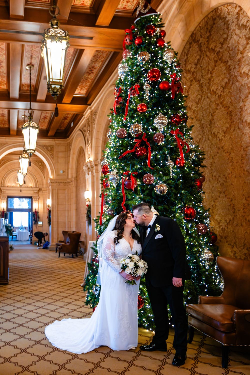Elegant wedding ceremony setup in a grand hotel hallway with tall Christmas trees and decorative lighting.