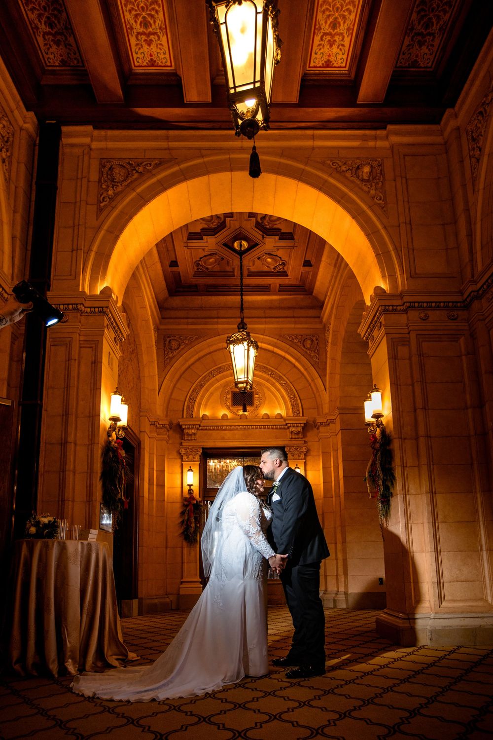 A wedding couple shares a romantic moment under ornate arches illuminated by vintage lanterns.