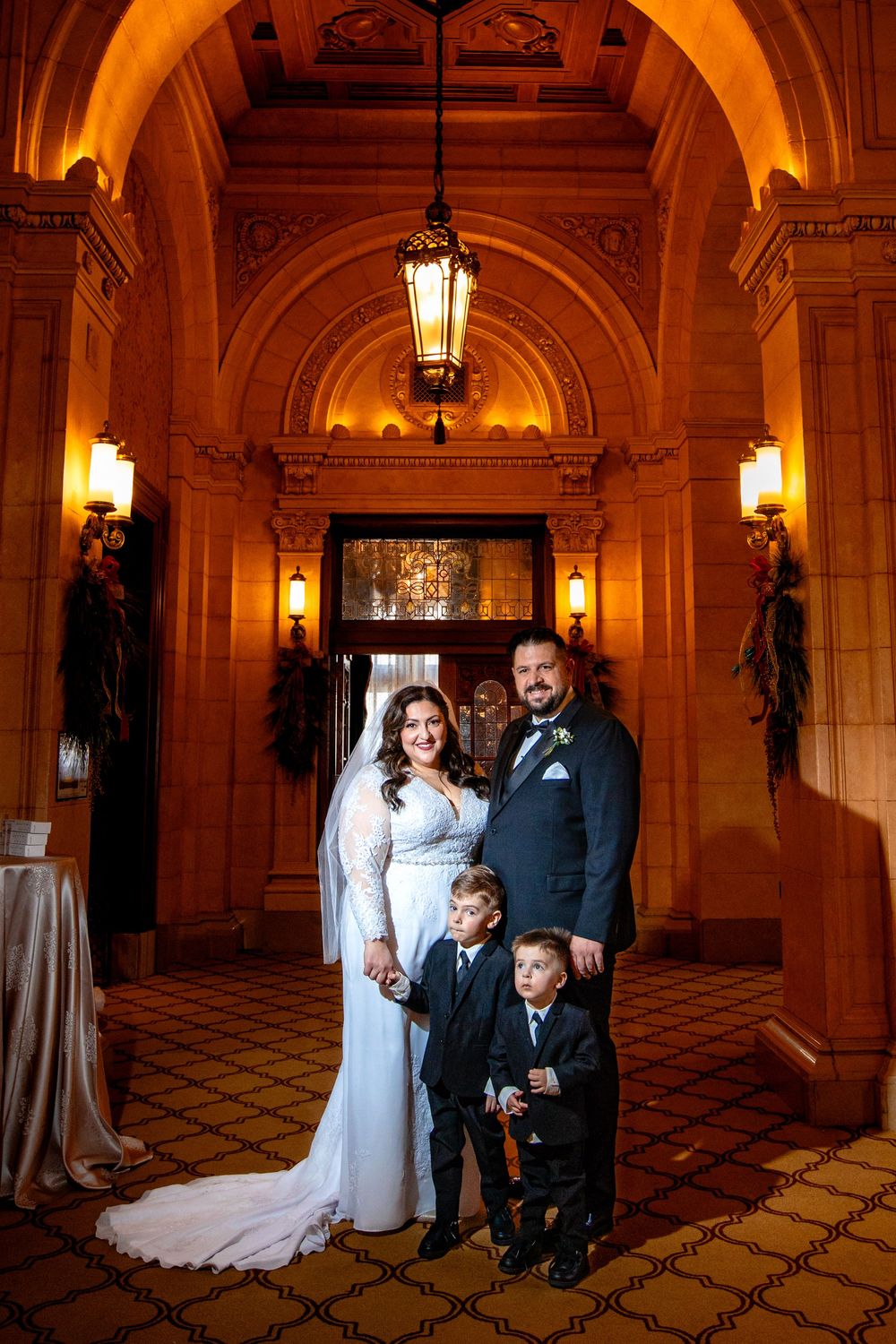 Elegant wedding portrait in an ornate historic venue with warm lighting and arched ceilings decorated with holiday greenery.