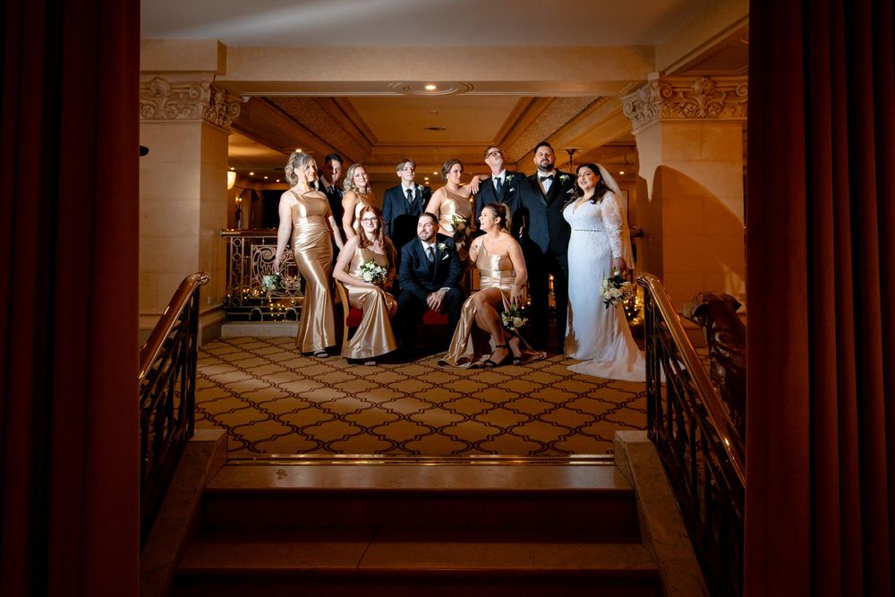 A bridal party stands in a beautifully lit church sanctuary with warm wooden pews and dramatic lighting.
