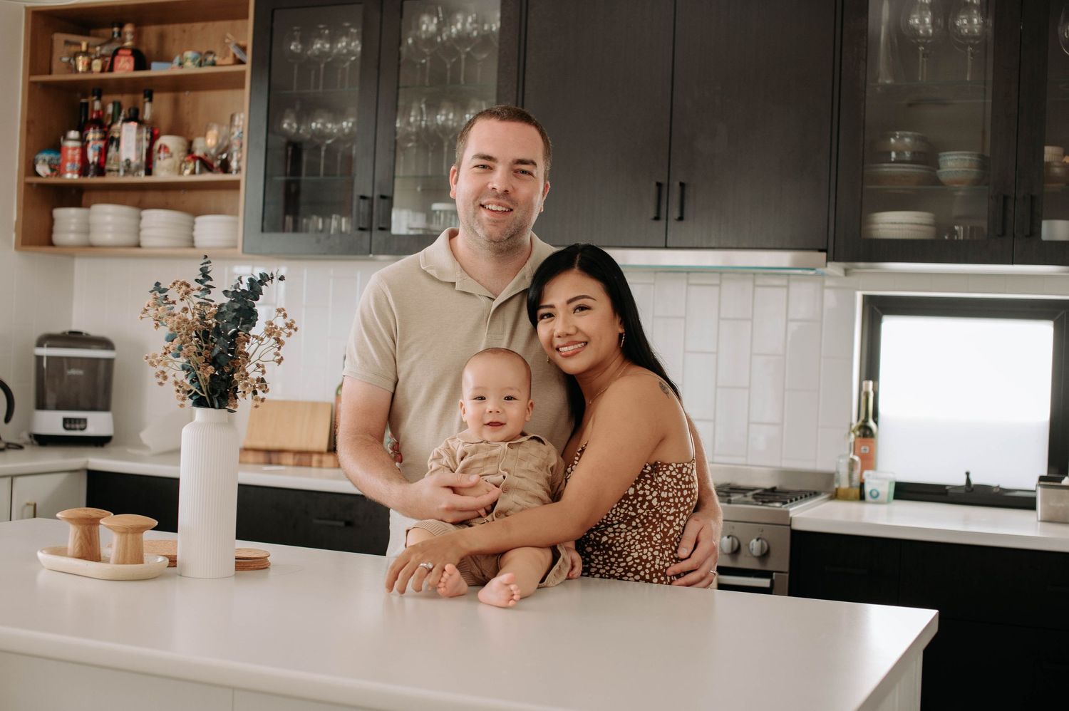 People sitting close together on a gray couch, smiling and embracing in a modern living room with hardwood floors.