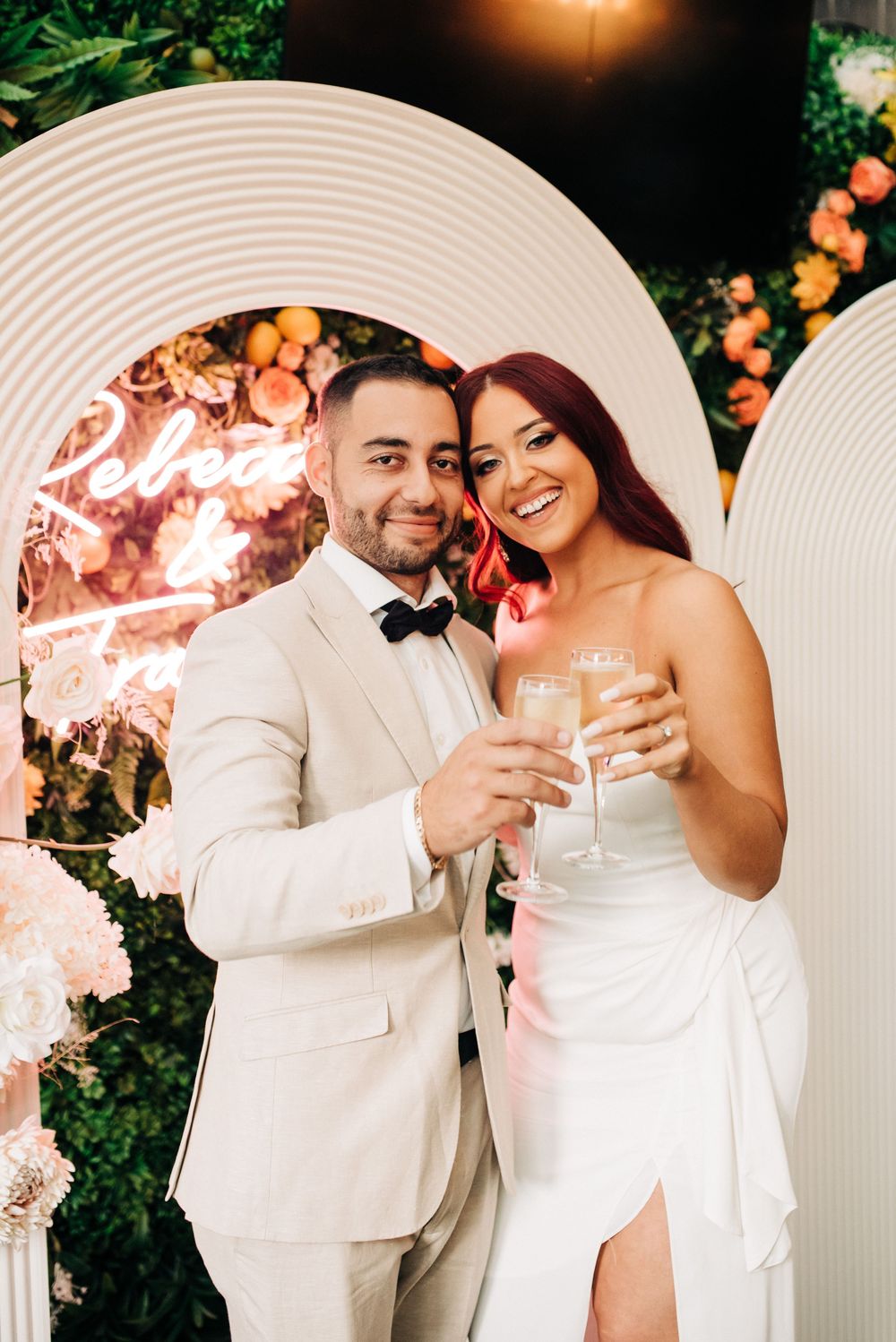 A wedding couple dressed in elegant white attire share romantic moments together in an outdoor garden setting.