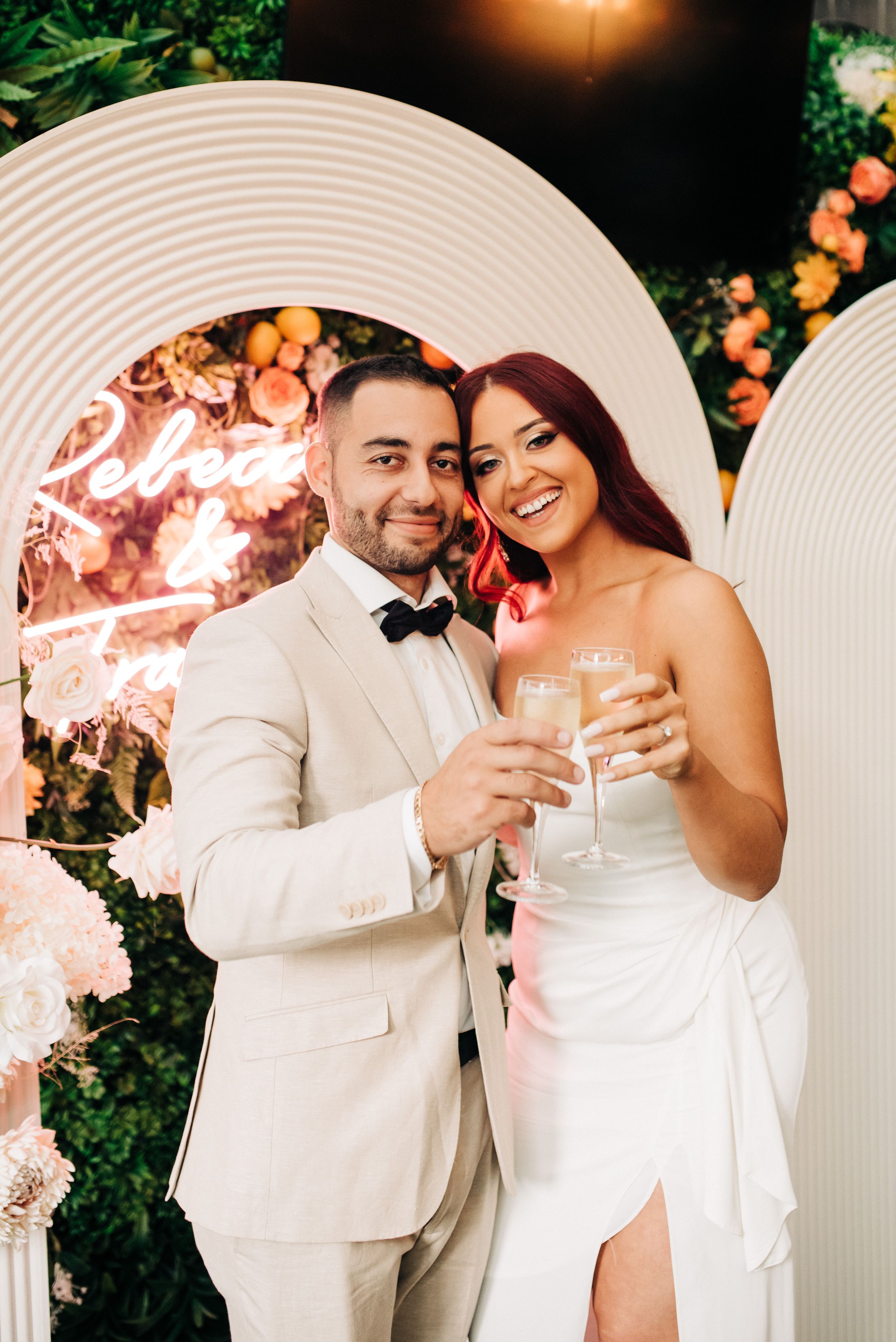 A wedding couple dressed in elegant white attire share romantic moments together in an outdoor garden setting.