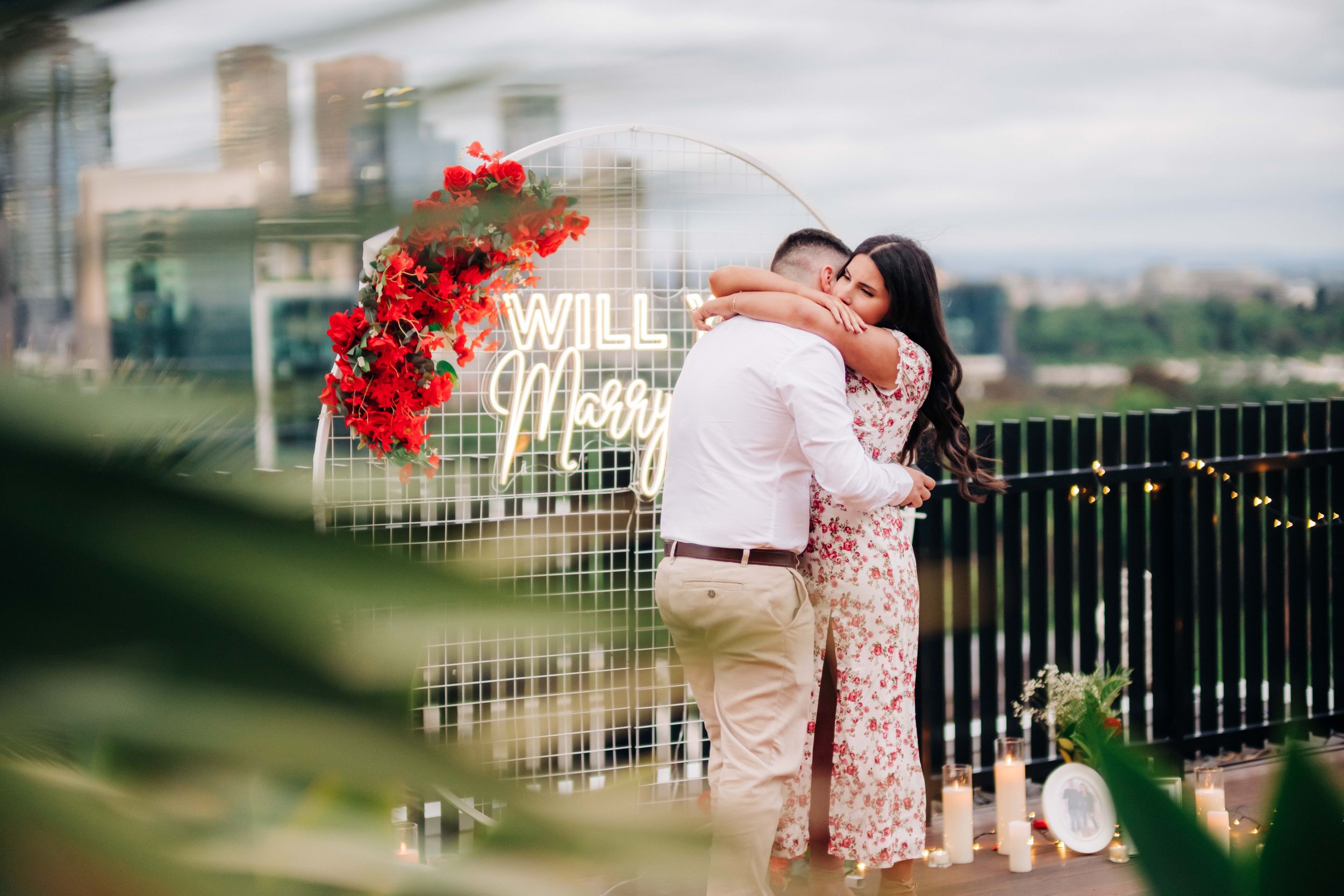 A montage of romantic engagement photos featuring red flowers and a park setting with the city skyline in the background.