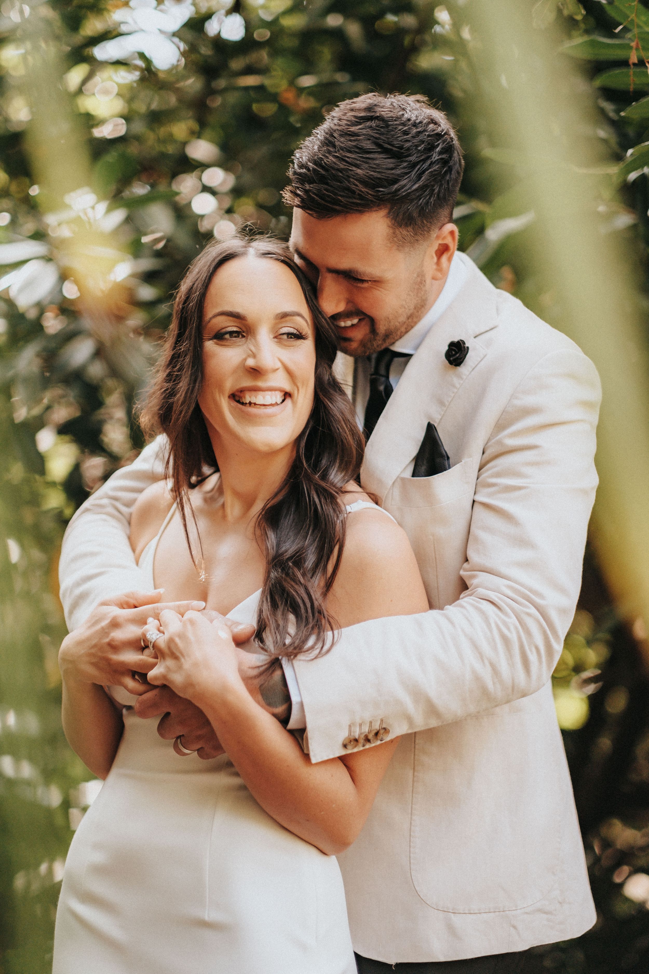 A romantic wedding couple embraces and shares joyful moments in a sunlit garden setting with bokeh effects.