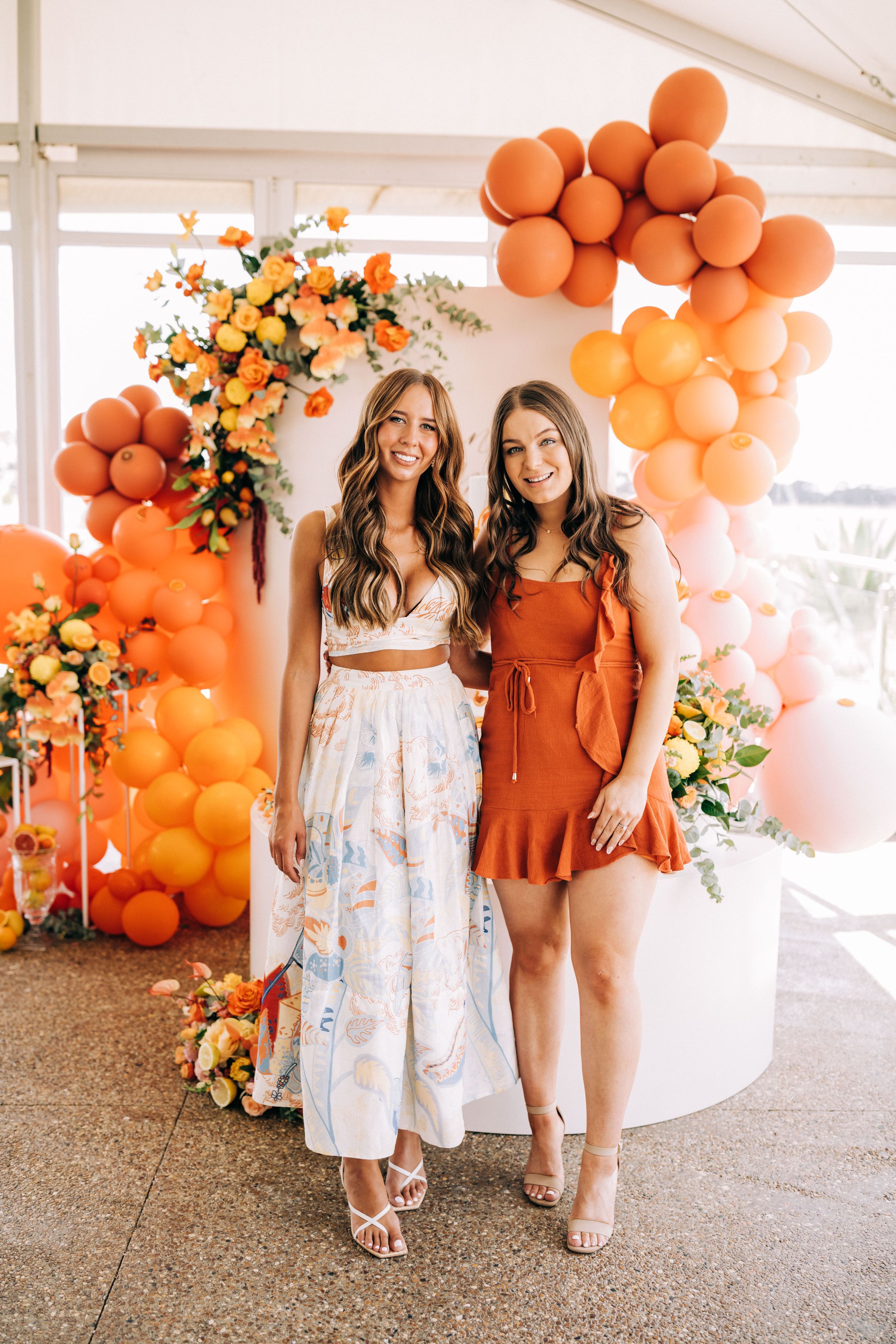 Orange balloon arch and floral decorations create a vibrant backdrop at an event with summer party dresses.