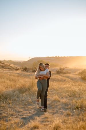 Romantic sunset moment captured between couple embracing on golden hillside trail.
