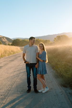 Couple poses together on dirt road during golden hour in countryside setting.