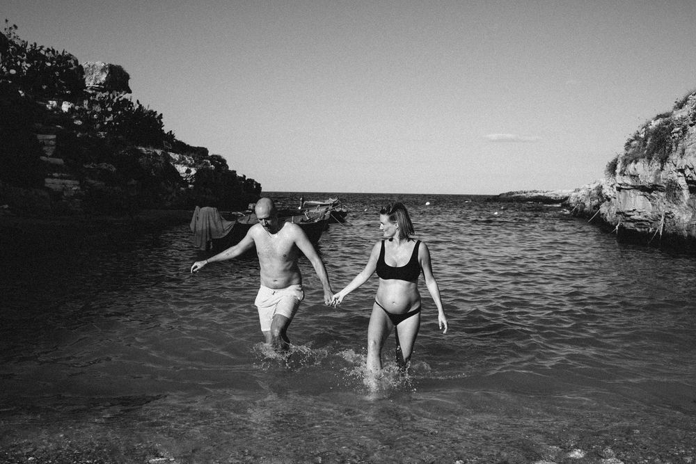 A sequence of black and white photographs showing people splashing and playing in the ocean along a rocky coastline.