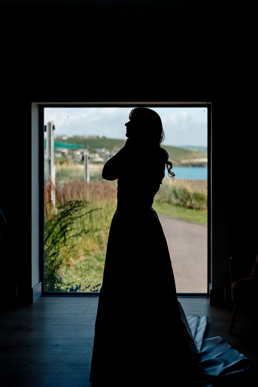 Silhouette of a person in a long dress standing in a doorway overlooking a coastal landscape.