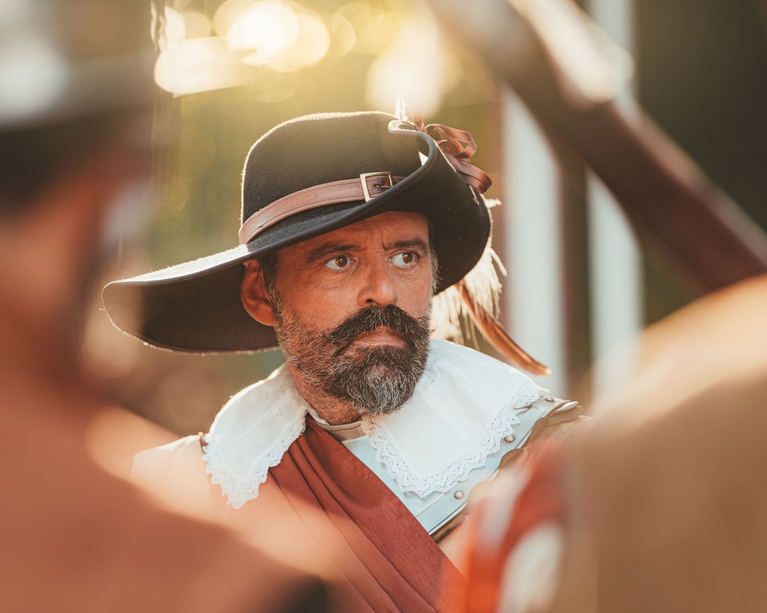 Row of people in historical dress and period hats viewed from a side profile.