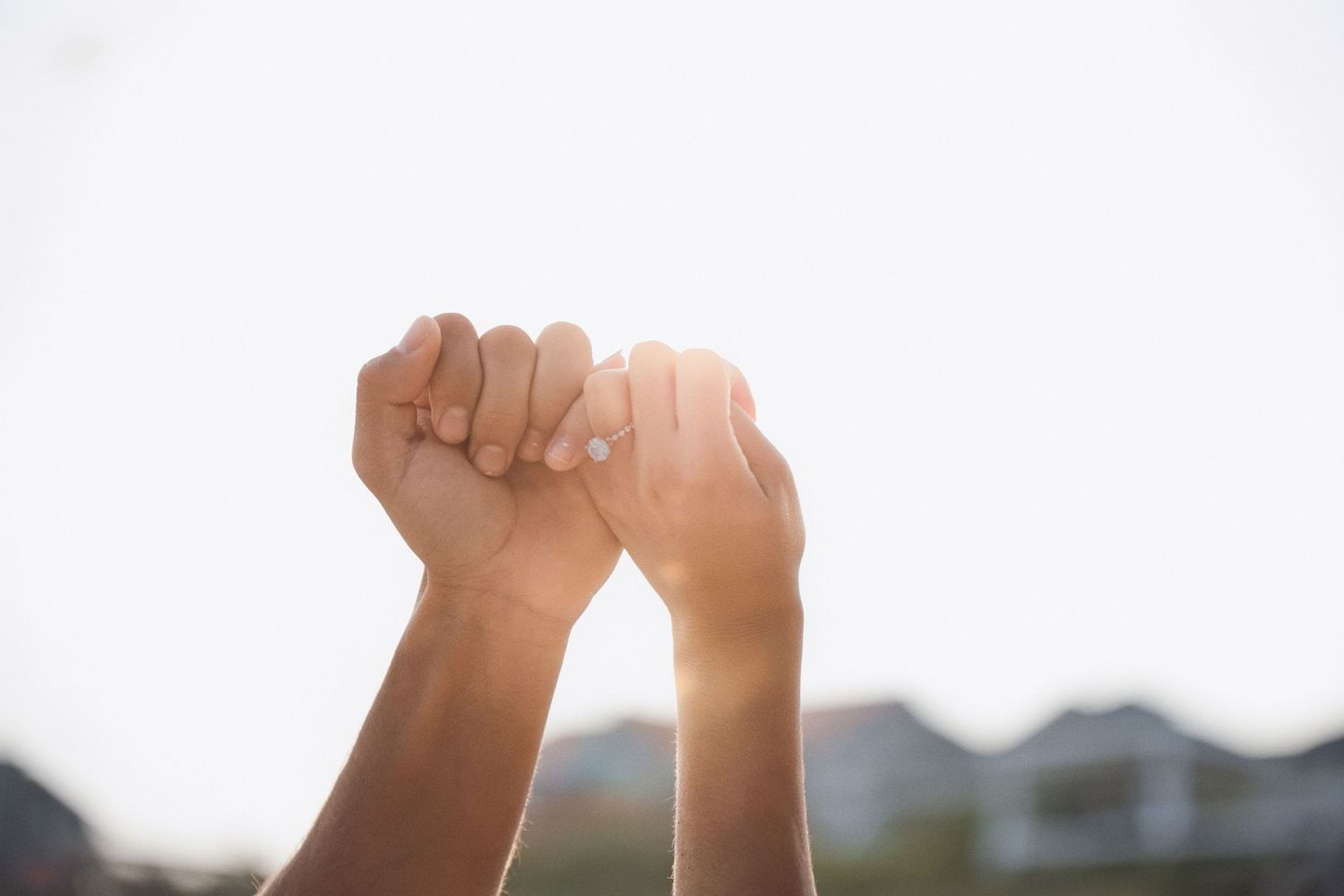 Two hands raised against a bright sky in a gesture of unity and celebration.