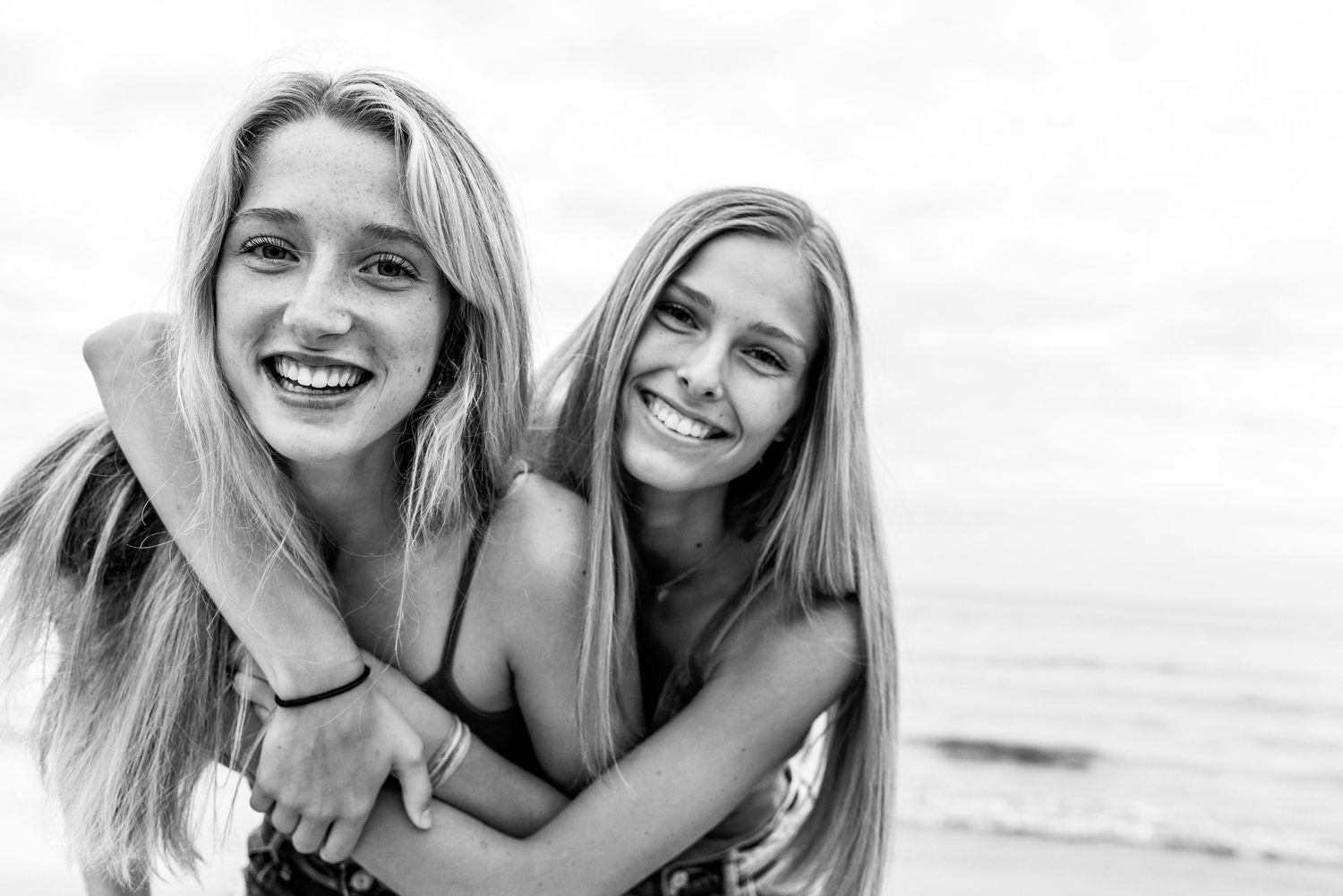 Two best friends sharing a joyful moment together at the beach in black and white photography.