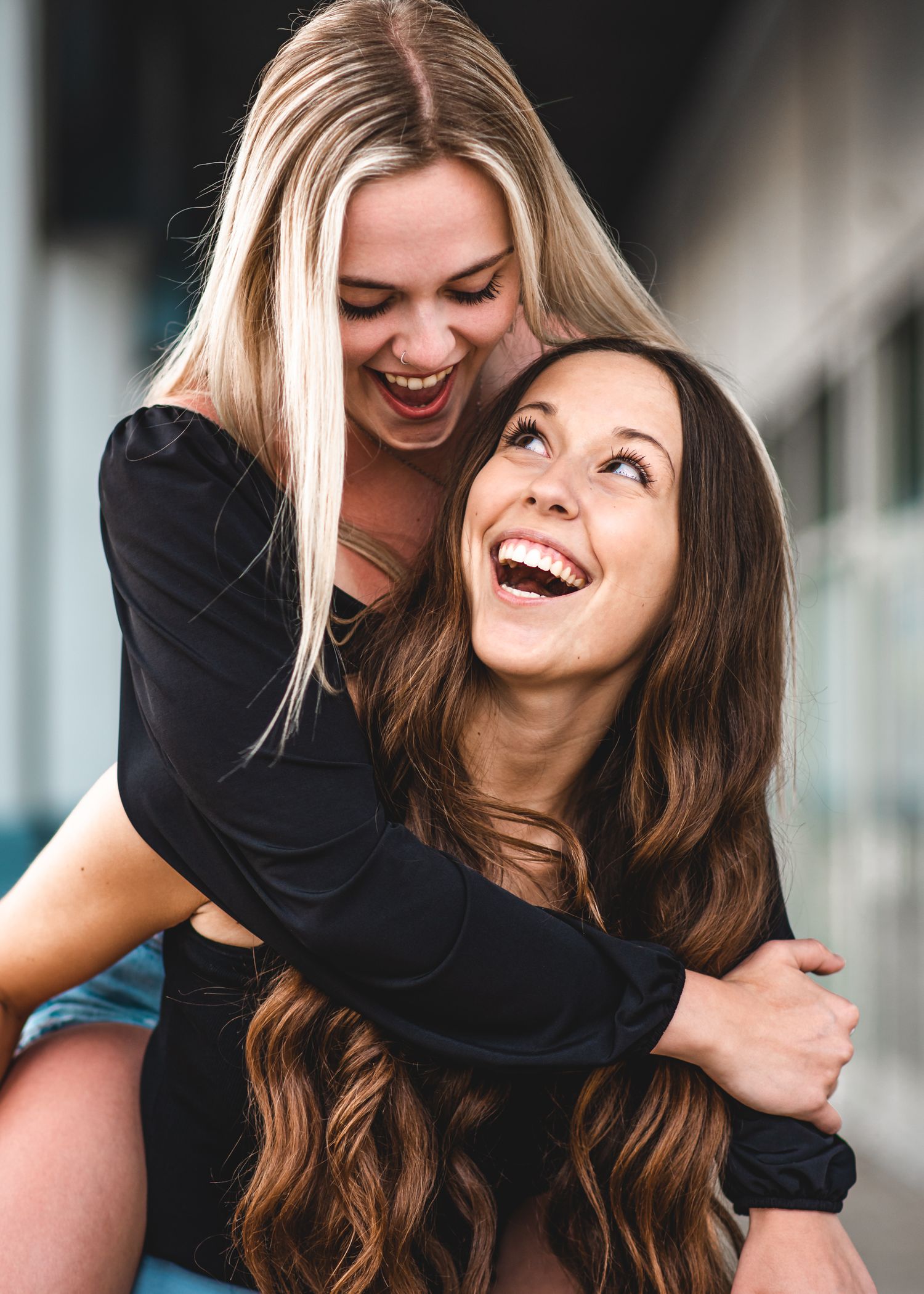 Two friends laughing and embracing while wearing black tops in a candid moment of joy and connection.