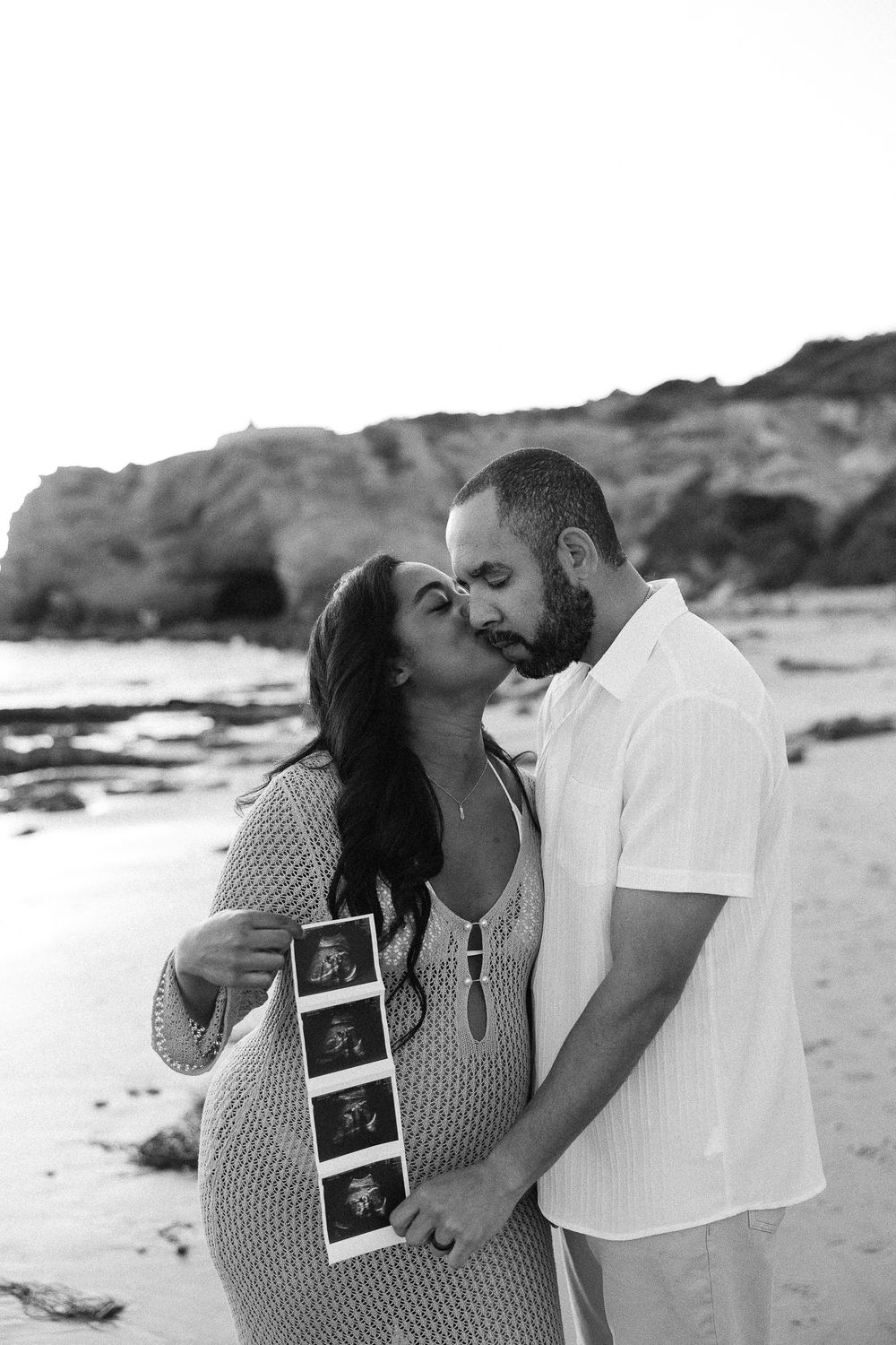 Black and white beach pregnancy announcement photos showing couple kissing while holding sonogram pictures.
