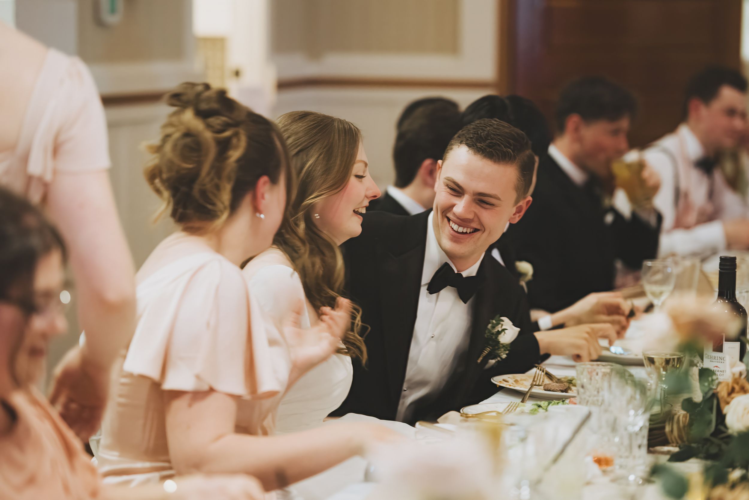 Wedding guests share a joyful moment during dinner at an elegantly decorated reception table.