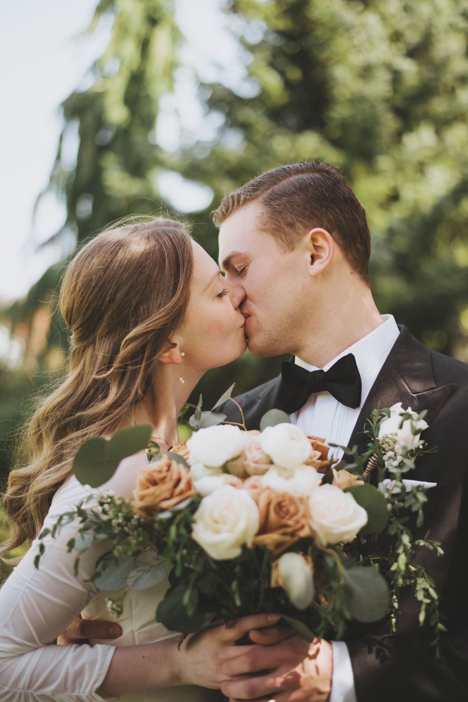 Couple in wedding attire embraces with pink azalea bushes blooming in the garden background.