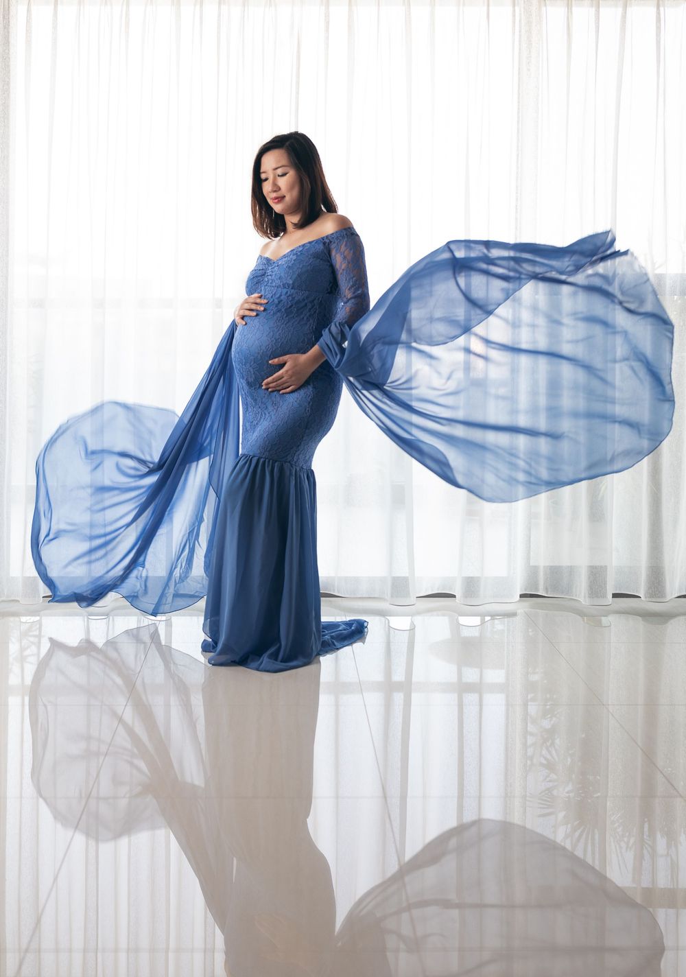 Flowing blue maternity dress creates ethereal movement against white backdrop in artistic pregnancy photo sequence.