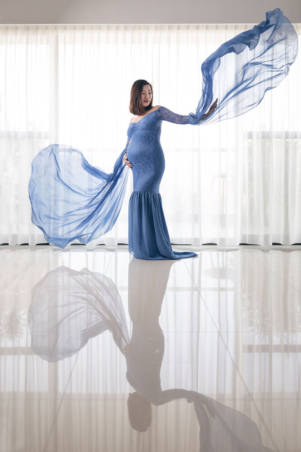 A figure in a flowing blue dress twirls gracefully against a bright white background creating ethereal fabric movement.