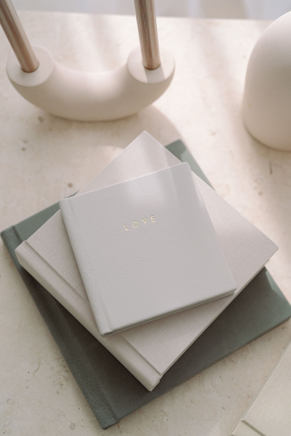 Minimalist flat lay composition of light gray and sage green notebooks stacked on white surface with soft shadows.