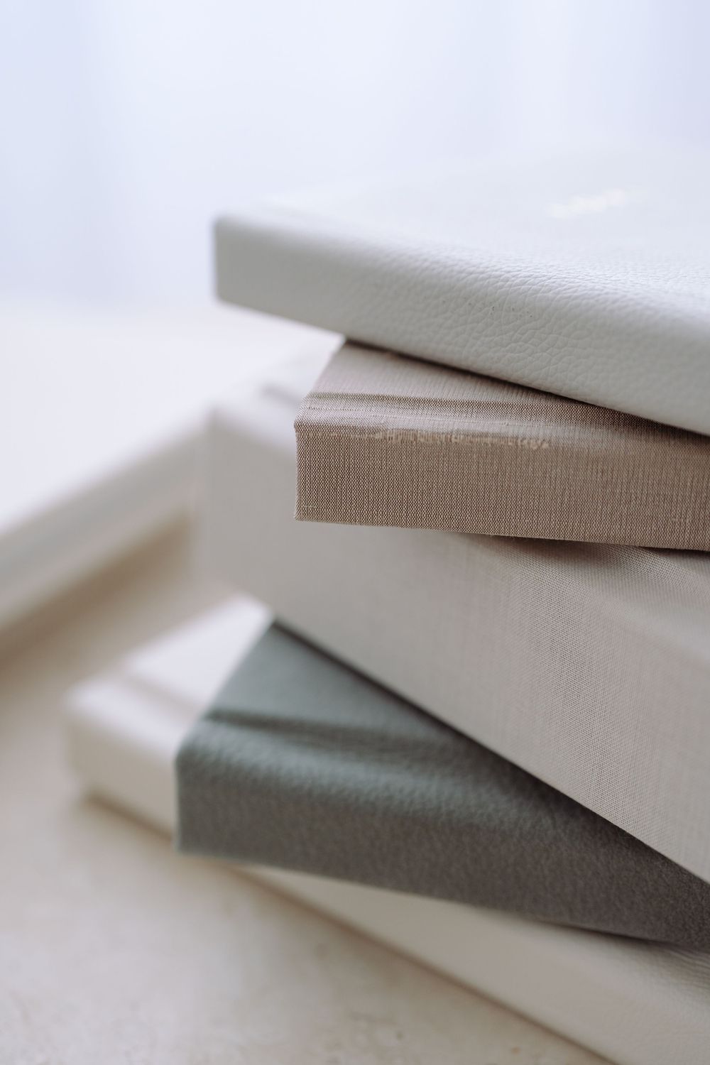 Stack of soft gray and white canvas books or photo albums arranged in a minimalist composition.