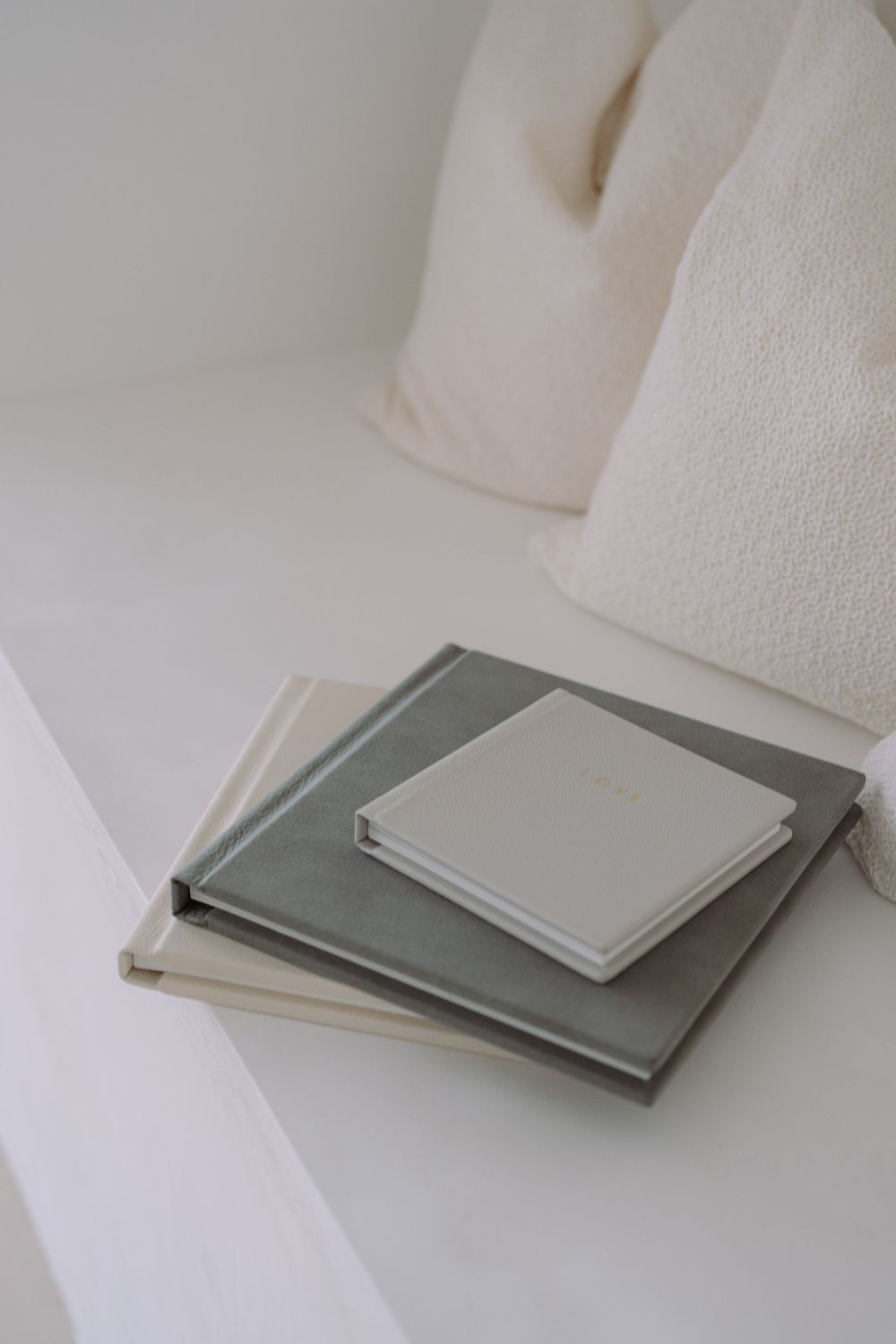 A stack of minimalist photo albums or books in neutral gray and cream colors sits on a white surface.