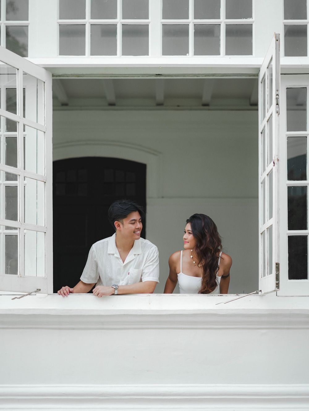 A couple shares a romantic moment while sitting at a bright white window in a sequence of three connecting photos.