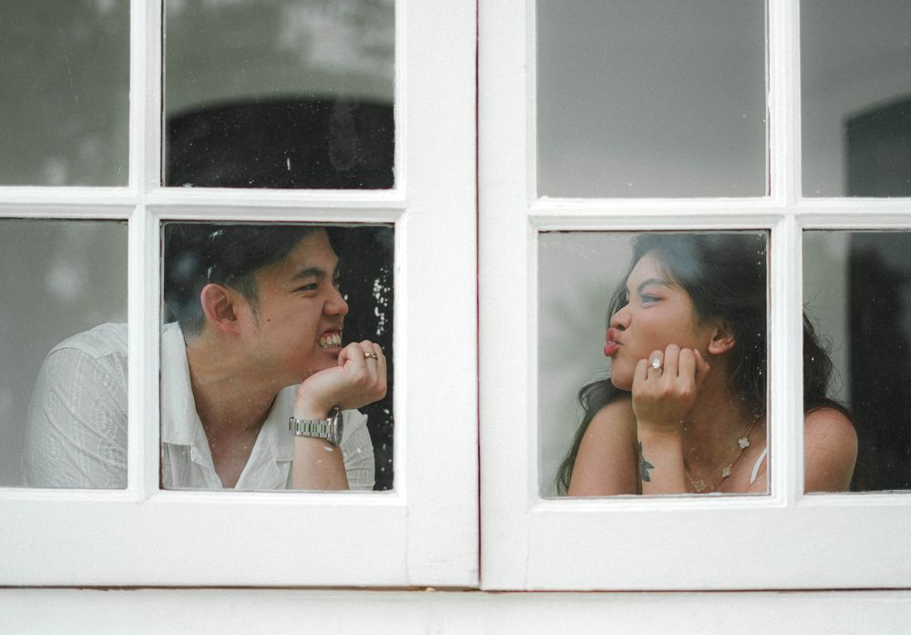 Through a white window frame, two people gaze at each other in a tender romantic moment.