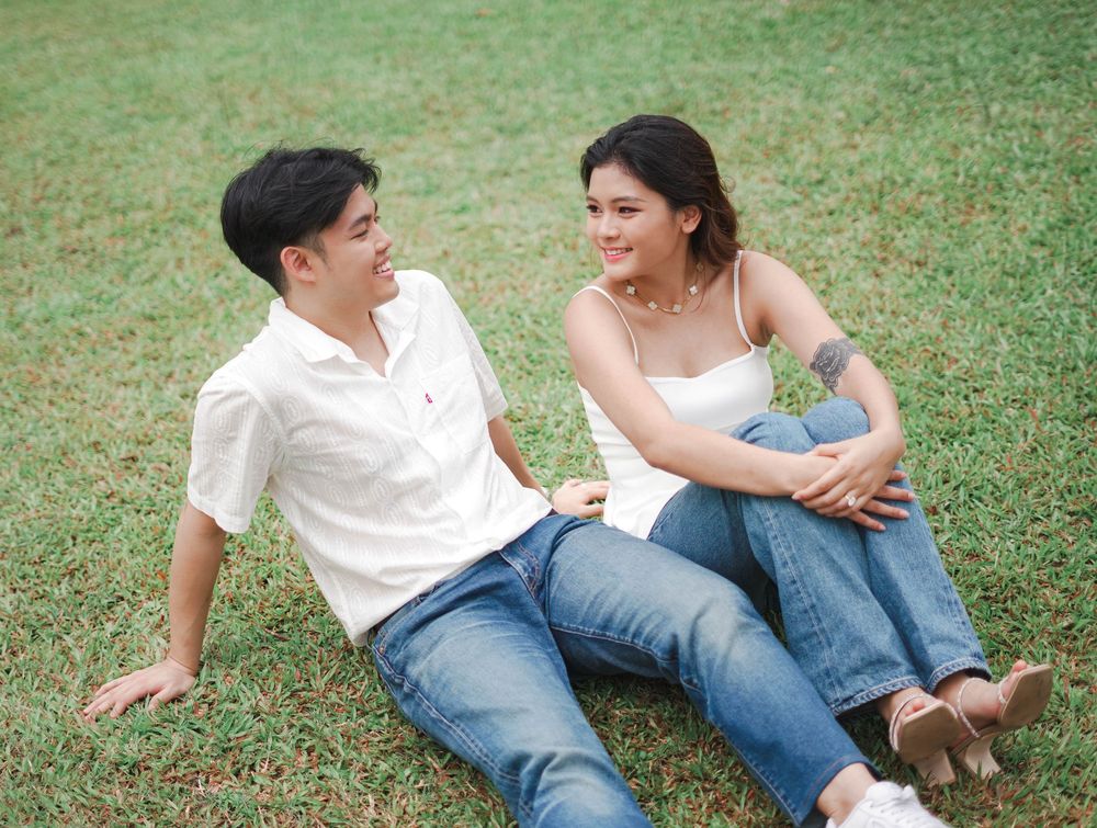 A couple in casual white and denim outfits relaxing together on green grass during a sunny day.