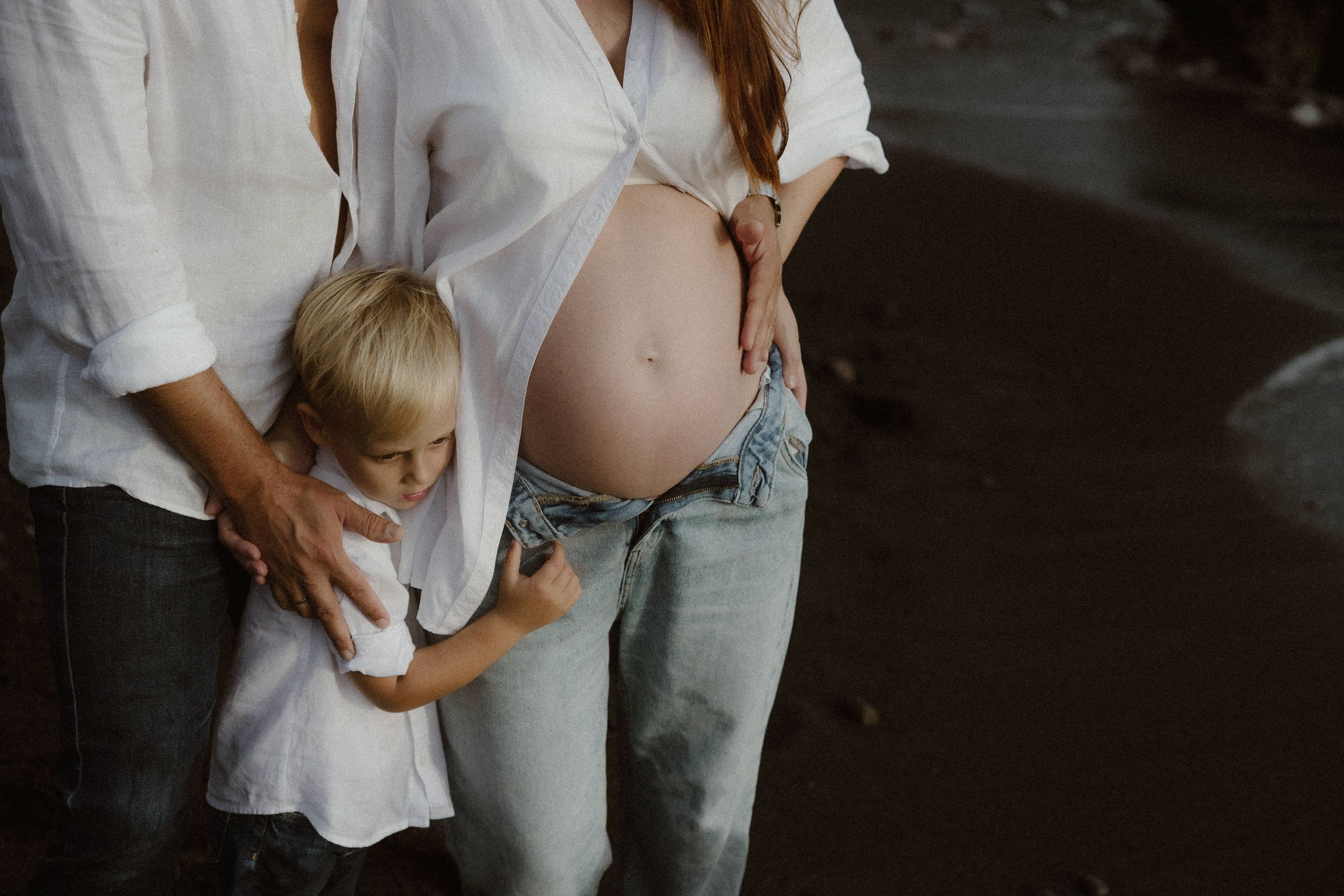 A series of photos showing a pregnant woman's growing belly over time in white shirt and jeans against a dark background.