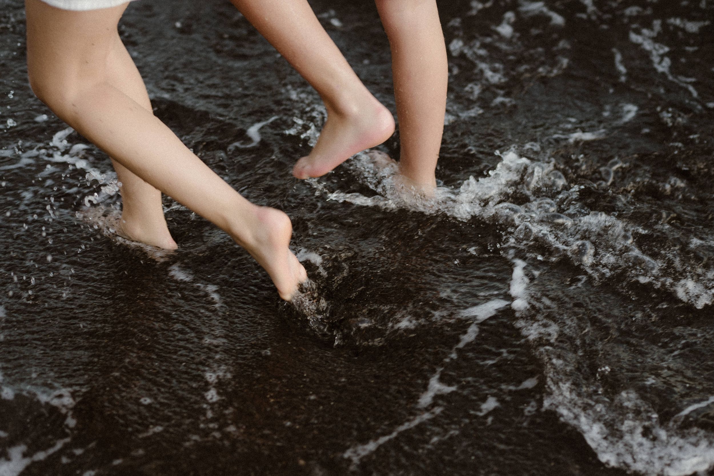 Bare feet splashing in shallow water creating ripples and reflections on a dark wet surface.