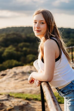 Young woman in casual attire poses outdoors at sunset against a mountainous landscape with glowing backlighting.