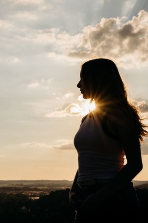 Silhouette against dramatic sunset sky with sunburst effect on mountaintop.