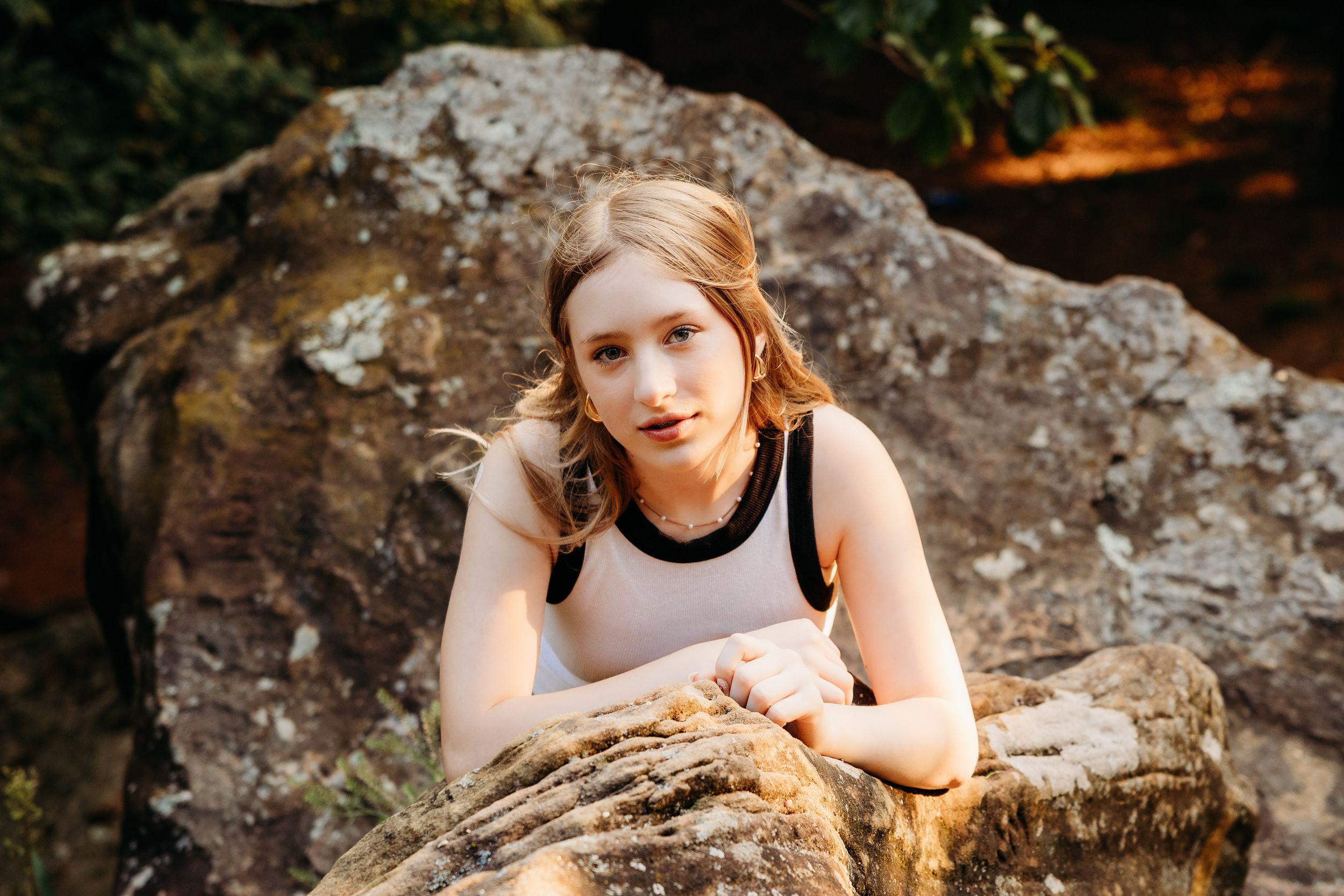 A person in a sleeveless top leans on a large rock formation during golden hour lighting outdoors.