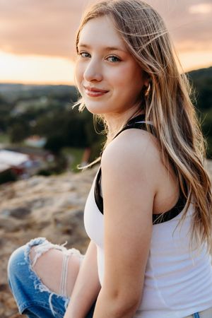 A series of photos depicting someone wearing a white tank top and jeans in golden sunset lighting on a hilltop.