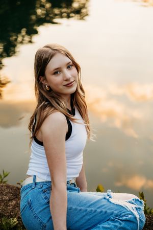 A casual outdoor portrait in a white tank top and blue jeans at sunset with warm golden lighting.