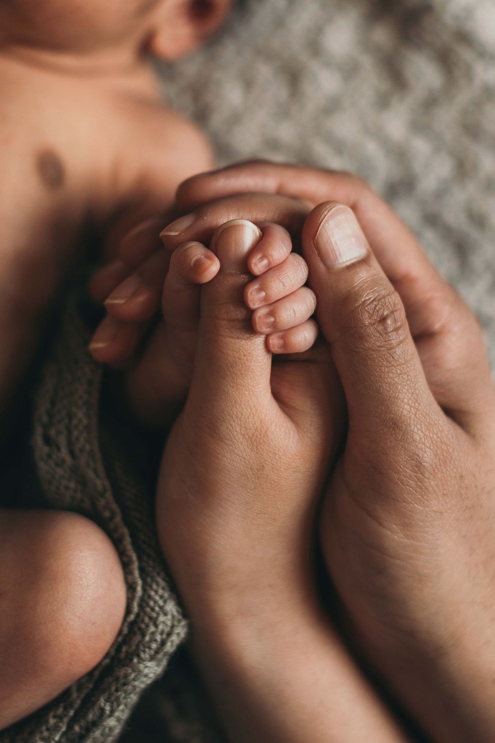 Newborn-kuvaus kotona. Yksityiskohta vauvan ja vanhempien käsistä. Valokuvaaja Annina Nygård, pääkaupunkiseutu ja Uusimaa.