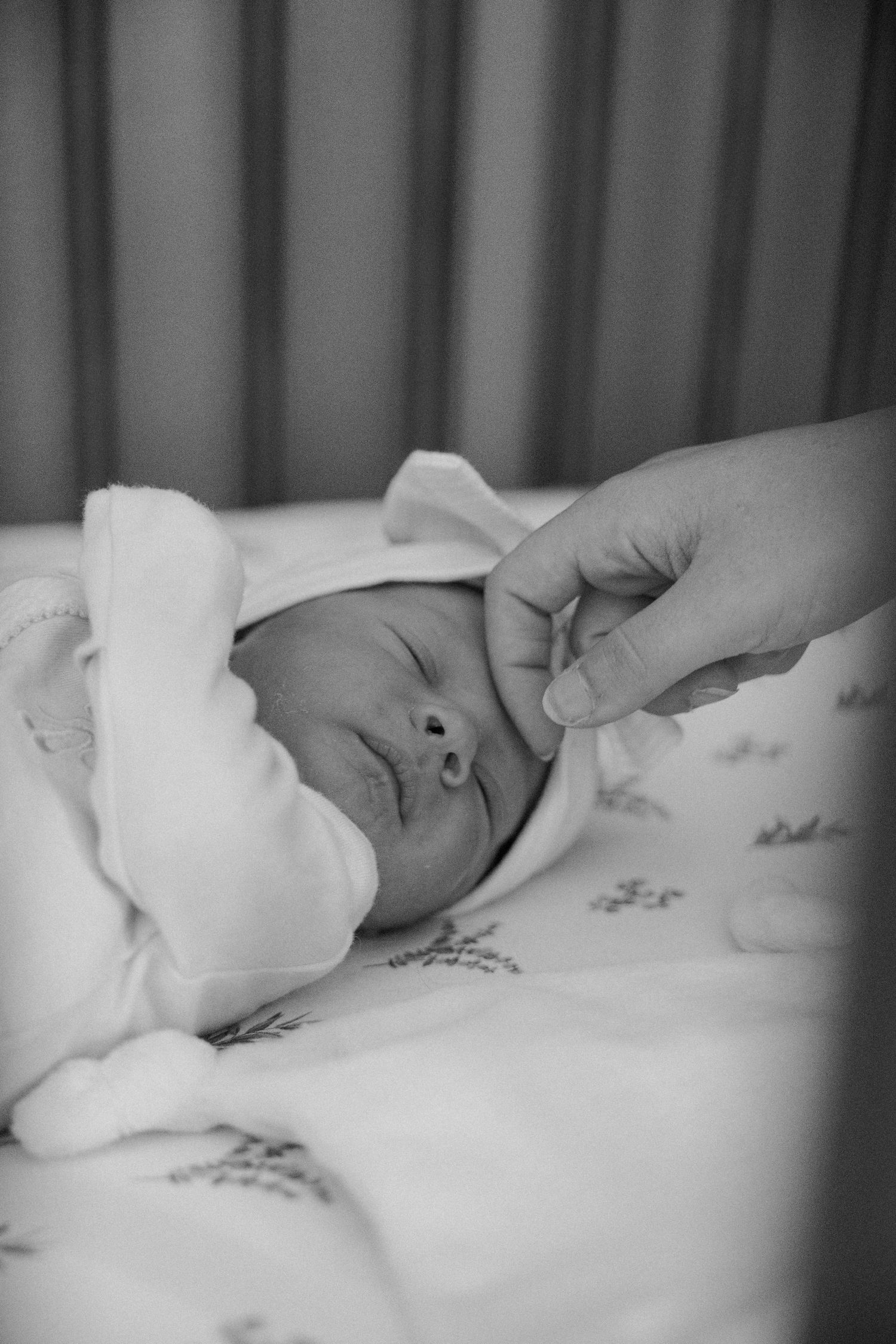 A black and white photograph of a newborn baby swaddled in a blanket resting on floral patterned bedding.