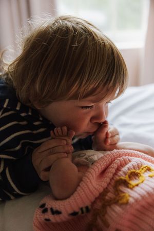 A small child in a striped shirt rests on a pink knit blanket in a soft, dreamy lighting setting.