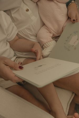 Close-up view of hands writing or drawing in a white notebook on a light surface.