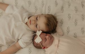 A sleeping infant rests peacefully on soft bedding with delicate floral wallpaper in the background.