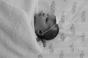 Baby sleeping peacefully on white bedding with delicate floral pattern details.