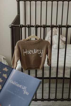 A series of photos showing a brown knitted sweater hanging on dark crib bars with a blue book in the foreground.