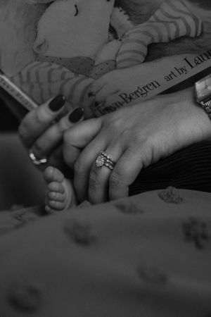 Black and white close-up photo showing hands with engagement ring resting on a surface.