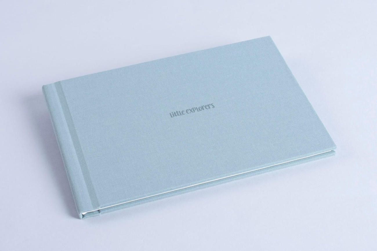 Wedding photo album with brown and cream pages lies open on a textured grey surface next to coffee and sweets.