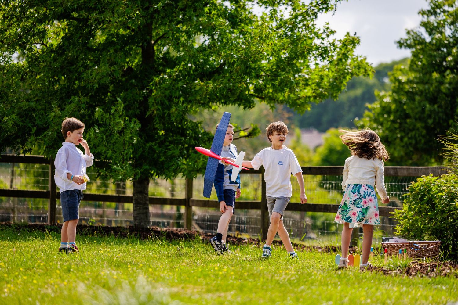 A group of people participate in an outdoor game of cornhole or bean bag toss on a sunny summer day.